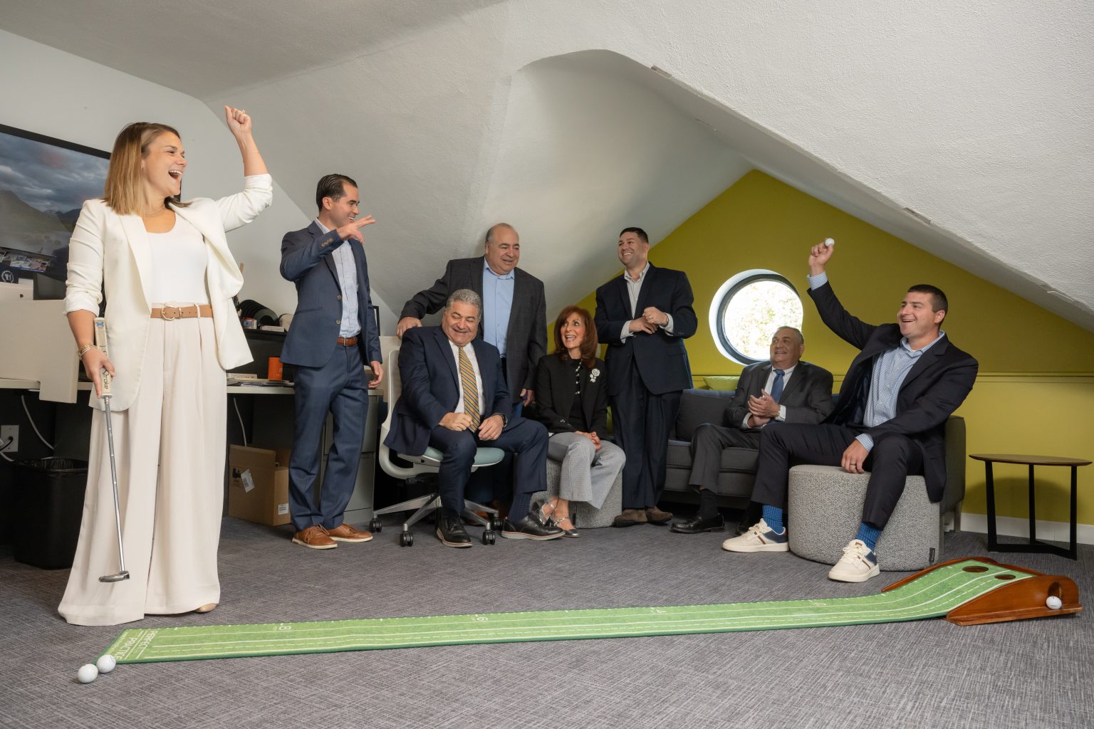 Jenna makes a golf putt on an indoor mat while the team celebrates.