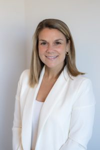 A profile photo of Jenna Figueiredo wearing a white blazer and a soft white background