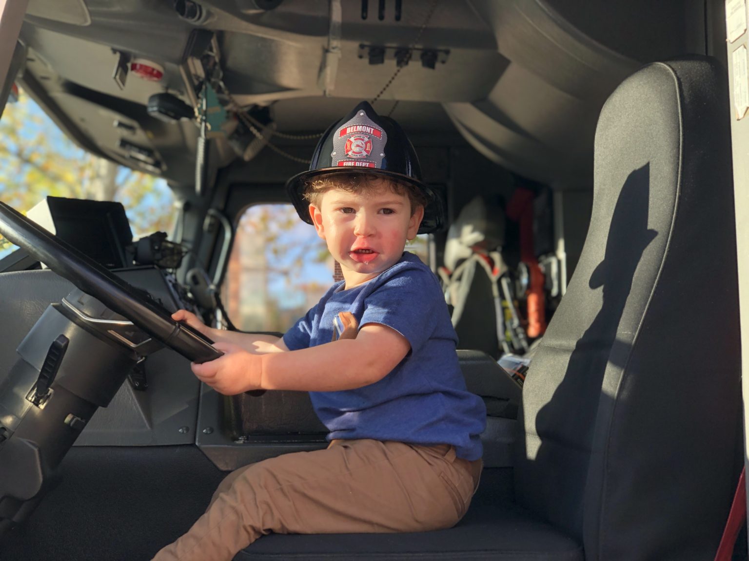 A photo of a child sitting in the driver's seat of a fire engine at Belmont Fire Department's Touch A Truck Event