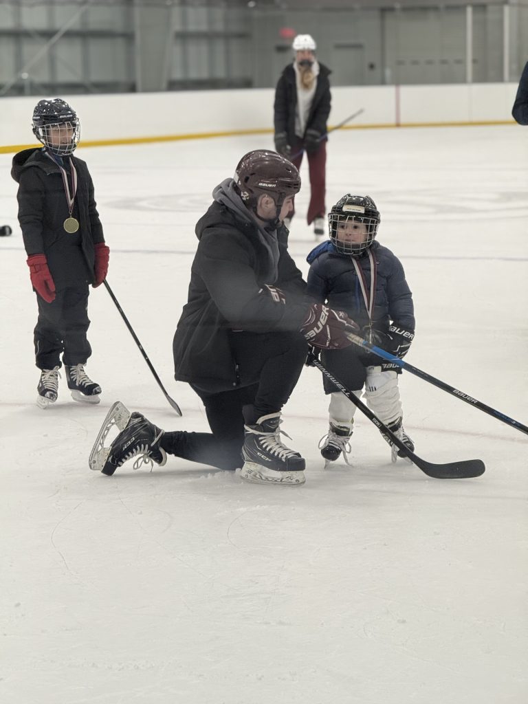 A photo of a coach at Belmont's Learn to Skate Program chatting with a skater dawning a medal at the programs conclusion