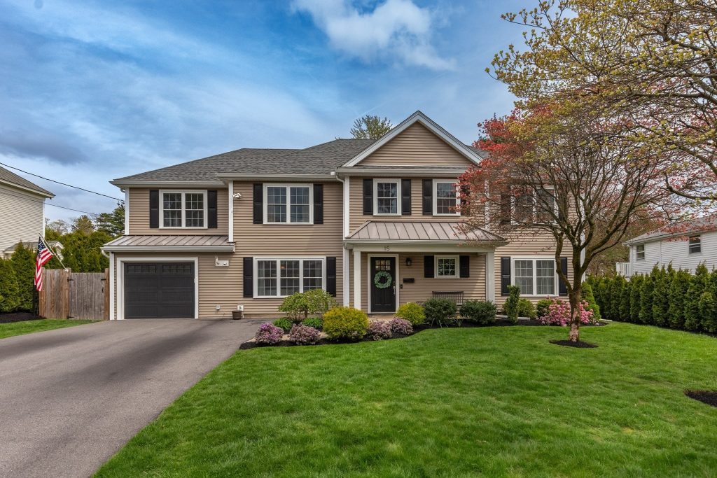 a listing photo picturing the front view of a 4 bedroom colonial with green manicured lawn and plantings