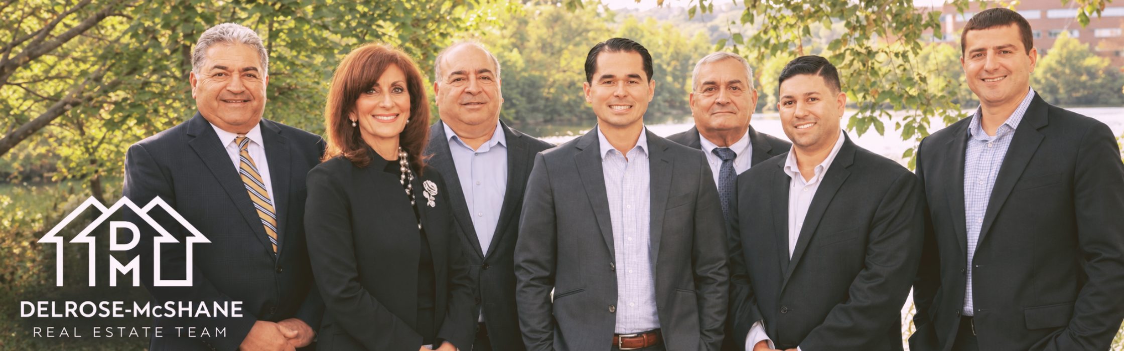 A photo of the DelRose McShane Team posing in front of a pond with the team logo in the lower left-hand corner of the banner image