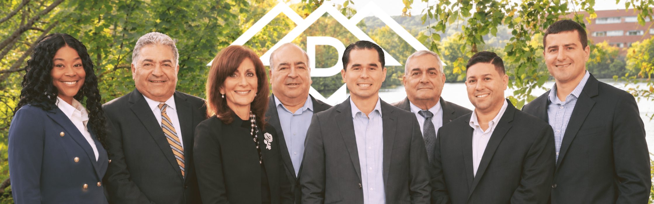 A photo of the DelRose McShane Team of Coldwell Banker Realty posing for a photo in front of Claypit Pond in Belmont Massachusetts with the Team Logo superimposed in the background.